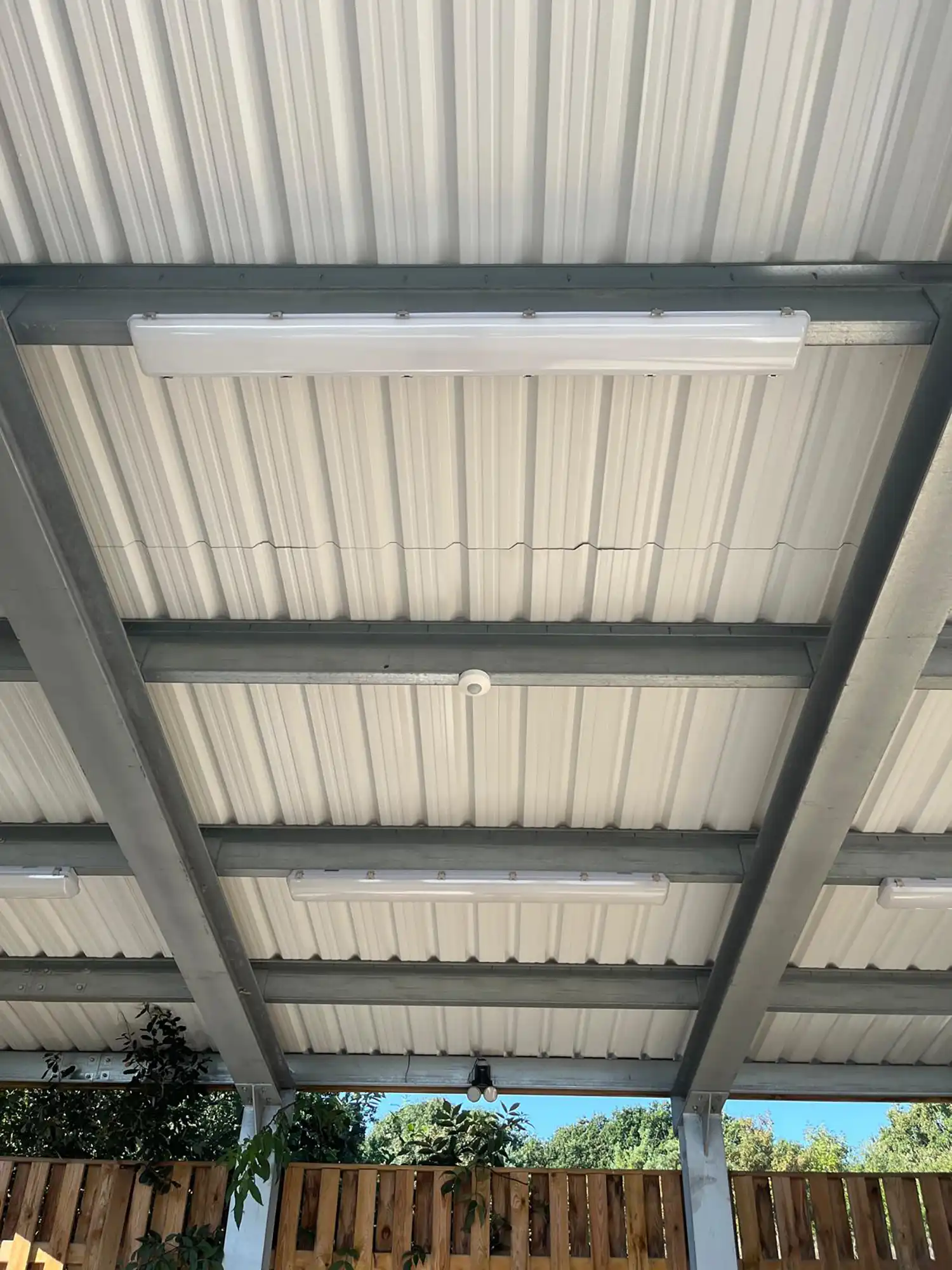 A patio covered in a metal roof next to a wooden fence.